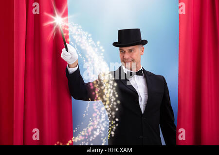 Happy Mature Magician Wearing Black Hat Doing Magic With Illuminated Wand Stock Photo