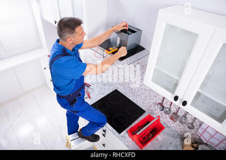 Elevated View Of Male Technician Checking Extractor Filter With Digital Multimeter In Kitchen Stock Photo