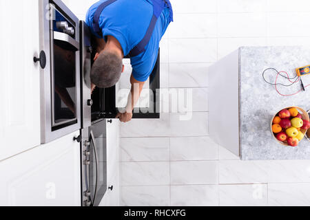 Mature Technician In Overall Repairing Oven In Kitchen Stock Photo