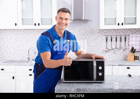 Mature Man Repairing Microwave Oven In Kitchen Stock Photo