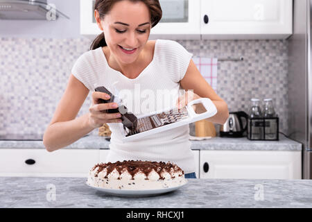 Portrait Of A Smiling Young Woman Grating Chocolate Over Cake Stock Photo