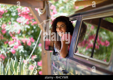 Young woman in a camper van in a beautiful camping with pink flowers Stock Photo