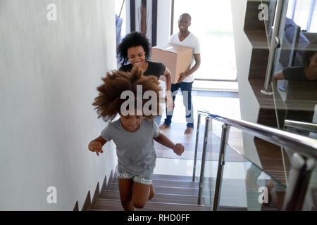 Happy black child running upstairs moving with parents holding boxes Stock Photo