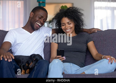 Happy black couple with pet laughing looking at smartphone Stock Photo