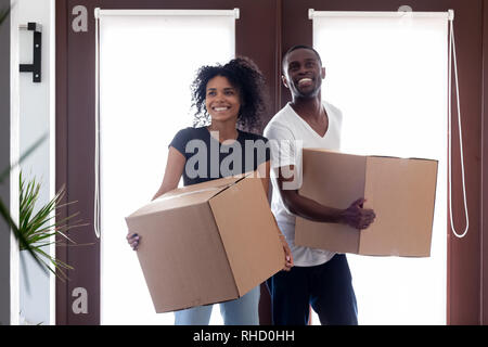 Excited black couple carrying boxes entering big modern house hallway Stock Photo