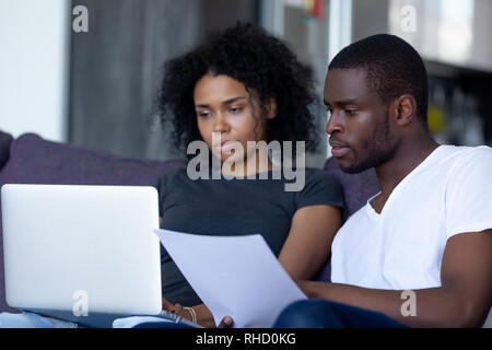 Serious african couple pay bills online on laptop at home Stock Photo