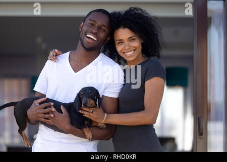 Happy african millennial couple embrace outdoors holding pet, portrait Stock Photo