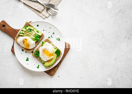 Avocado Sandwiches with Poached Eggs - sliced avocado and egg on toasted bread for healthy breakfast or snack, copy space. Stock Photo