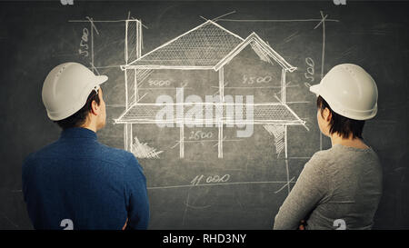 Construction engineers man and woman wearing protective helmet sharing thoughts together drawing a house plan project on blackboard. Idea exchange, wo Stock Photo