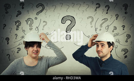 Confused man and woman engineer have the same common questions as drawn interrogation marks and mess goes out of head. Puzzled workers having problems Stock Photo