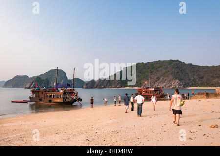 Tourists getting ready to leave on the beach with wooden junk boats anchored by the shoreline, Ha Long Bay, Vietnam Stock Photo