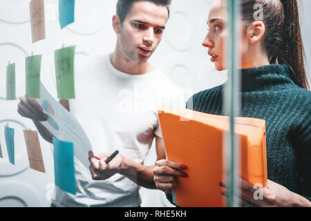 Team of project managers having meeting at modern office. Business colleagues discussing new ideas and using sticky glass note wall Stock Photo