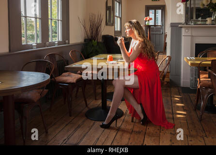 Lady in red dress sitting in Roydon Station, Restaurant, Essex Stock Photo