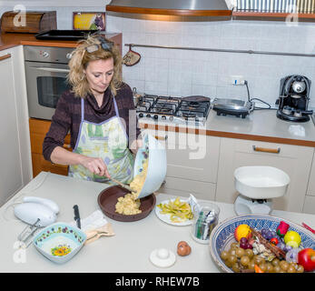 Housewife pours the dough into the mold to prepare a cake in a messy kitchen Stock Photo