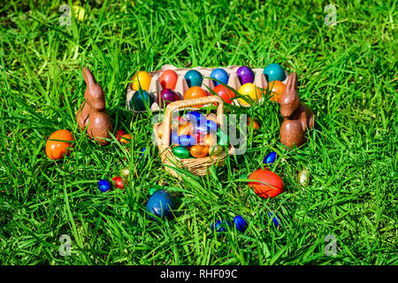 Chocolate Easter bunnies, straw basket full of colourful eggs on green grass Stock Photo
