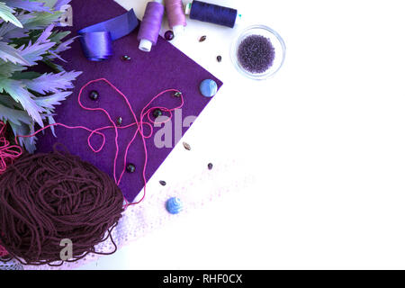 Materials for needlework in violet color on a white background. Beads, threads and wool for knitting Stock Photo
