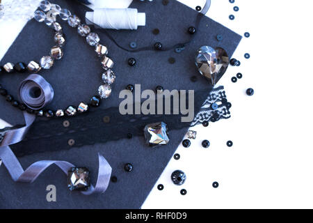 A set of materials for needlework in grey color on a white background. Beads, threads, a satin ribbon. Stock Photo