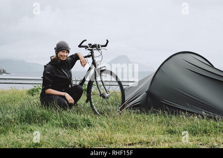 Portrait of a young woman bikepacker cyclist with her tent and bicycle in the Faroe Islands. Stock Photo