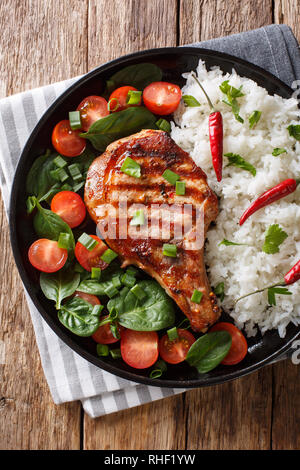 Healthy grilled pork steak with rice and fresh vegetables close-up on a plate on the table. Vertical top view from above Stock Photo