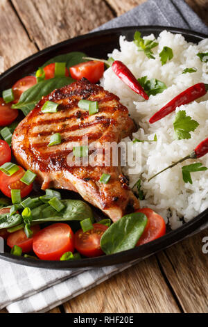 Grilled pork steak with rice garnish and fresh vegetable salad close-up on a plate. vertical Stock Photo