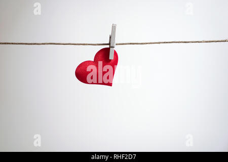 Single red heart hanging from string by clothes peg on white background. Romantic Valentine's Day scene with copy space.