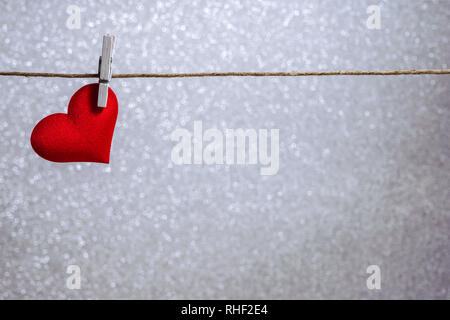 Single red heart hanging from string by clothes peg on silver background. Romantic Valentine's Day scene with copy space Stock Photo