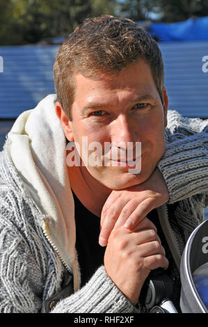 Portrait of a smiling Caucasian man in grey sweater with folded arms in sunny day Stock Photo