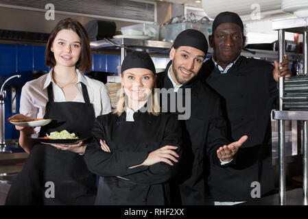 Positive multinational team of restaurant staff standing together in professional kitchen Stock Photo