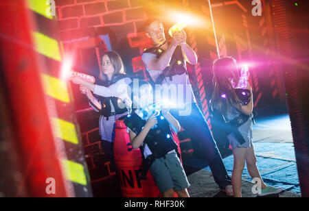 Group of happy kids and adults having fun on dark lasertag arena in colorful beams of laser guns Stock Photo