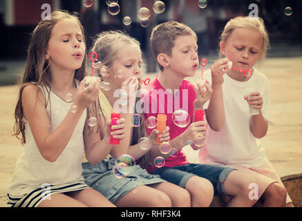 cheerful smiling boy and girls in elementary school age blowing bubbles outdoors Stock Photo