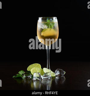 Elegant crystal cocktail glass with cold summer refreshing juicy drink, thin slices of lime, fresh green mint leaves and transparent ice cubes isolated on black background. Picture aspect ratio 1:1 Stock Photo