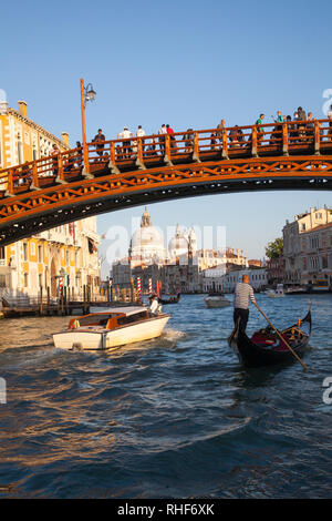 Accademia Bridge and Basilica di Santa Maria della Salute at sunset, Grand Canal, Venice, Veneto, Italy with gondola and water taxi passing under the 