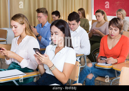 Students using smartphones to find necessary information on lecture in university class Stock Photo