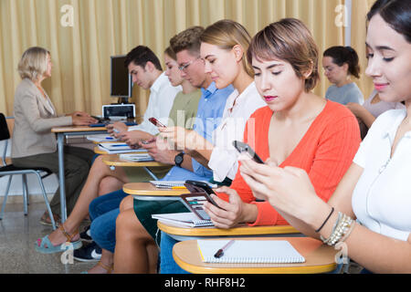 Students using smartphones to find necessary information on lecture in university class Stock Photo