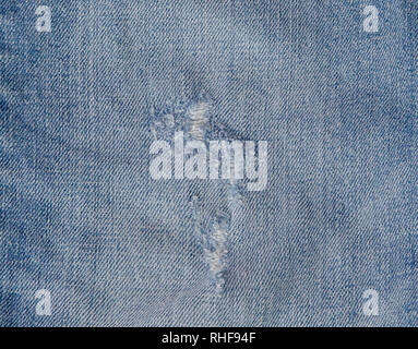 Hole and Threads on Denim Jeans. Ripped Destroyed Torn Blue jeans background. Close up blue jean texture. Stock Photo