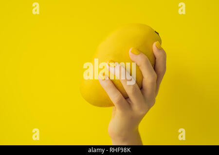 Hand with a yellow manicure holding a yellow ripe mango on a yellow background Stock Photo