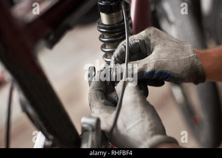 Cropped shot of male worker working in bicycle repair shop, repairing bike using special tool, wearing protective gloves Stock Photo