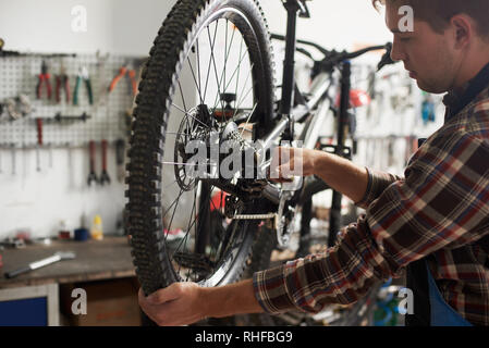 Man mechanic working in bicycle repair shop, technician repairing modern bike using special tool Stock Photo