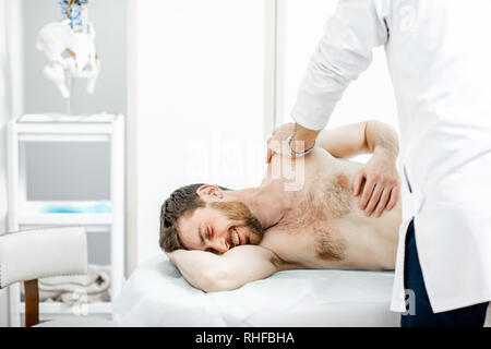Professional senior physiotherapist doing manual treatment to a man in the cabinet of rehabilitation clinic Stock Photo