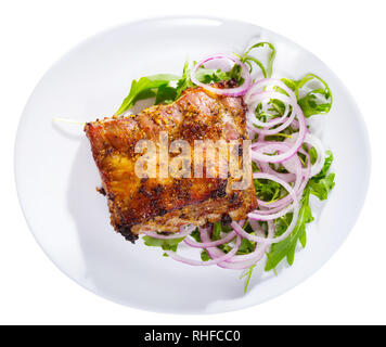 Juicy barbecue rack of pork served on fresh arugula with onion rings. Isolated over white background Stock Photo