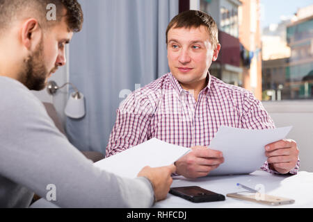 Portrait of two men in serious discussion at home table while analysing documents together Stock Photo