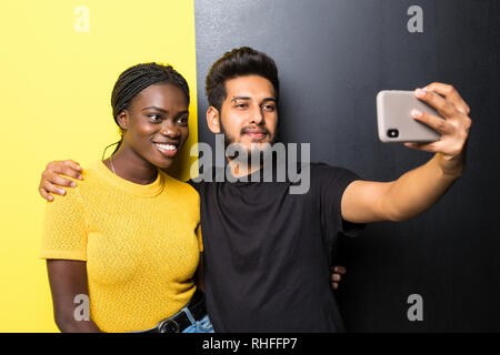 Young mixed race couple, indian man and african woman taking selfie while standing on different yellow and black background Stock Photo