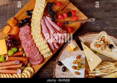 Decor of fresh cheese and meat crackers, green olives, nuts and berries on wooden gray boards Stock Photo