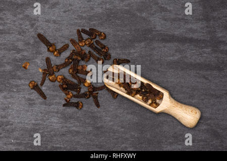 Lot of whole small dried cloves spice with wooden scoop flatlay on grey stone Stock Photo