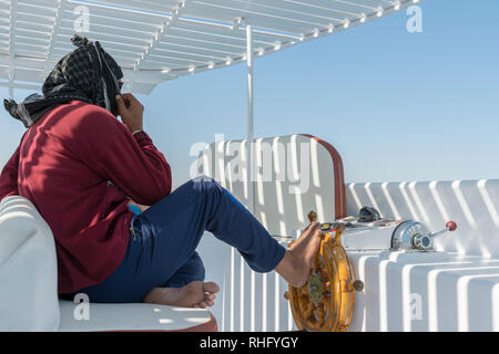 People at the helm of a white yacht. A man Arab controls the yacht. Foot on the yacht steering wheel Stock Photo