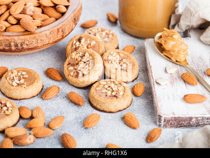 Homemade biscuit cookies with almond nuts and peanut butter on marble board on kitchen table background. Almonds in wooden bowl with jar and spoon of  Stock Photo