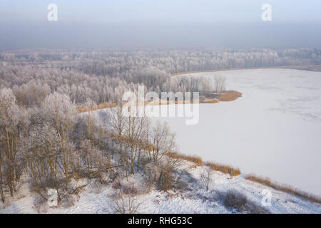 Rime and hoarfrost covering trees. Aerial view of the snow-covered forest and lake from above. Winter scenery. Landscape photo captured with drone. Stock Photo