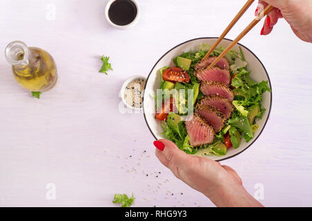 Japanese traditional salad with pieces of medium-rare grilled Ahi tuna and sesame with fresh vegetable salad on a plate. Plate with salad in hands. Au Stock Photo