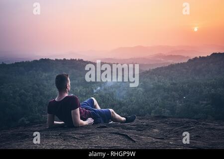 Young man contemplation on top of rock. Landscape at sunset in Sri Lanka. Stock Photo