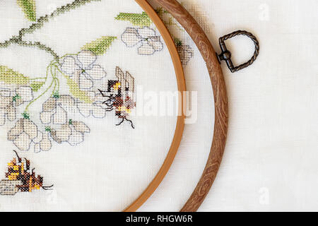 Wooden embroidery hoop with fragment of a colorful cross-stitch embroidery, summer flower ornament. Top view Stock Photo